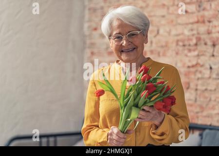 La femme âgée aux cheveux gris obtient de belles fleurs rouges pour la Journée nationale des grands-parents. Photo de haute qualité Banque D'Images