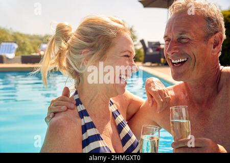 Couple senior retraité se relaxant dans la piscine pendant les vacances d'été célébrant boire du champagne Banque D'Images