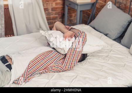 homme caucasien fatigué allongé sur son lit et couvrant son visage avec un oreiller blanc. Photo de haute qualité Banque D'Images