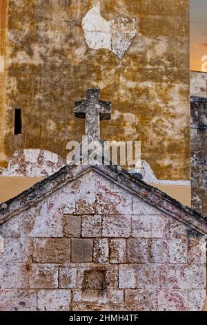 Croix de pierre sur un toit en face d'un mur méditerranéen de maison Banque D'Images