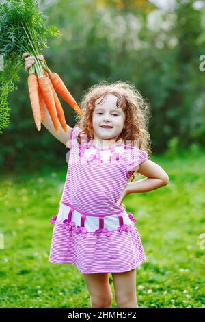 Petite fille avec carotte jaune dans le jardin. Banque D'Images