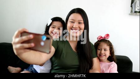 Mère asiatique prenant le selfie avec deux petites filles à la maison, tenant le smartphone Banque D'Images