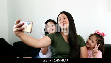 Mère asiatique prenant le selfie avec deux petites filles à la maison, tenant le smartphone Banque D'Images