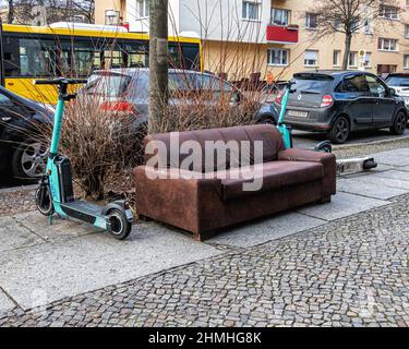 Jeté, abandonné, jeté, canapé en cuir et e-trottinettes électriques sur la chaussée à Gesundbrunnen, Berlin Banque D'Images