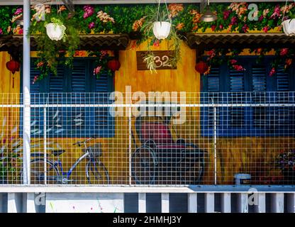 volets, maison en stuc avec des pots suspendus, un vélo assis à côté d'un mur peint murale tout derrière une clôture de grille. Banque D'Images