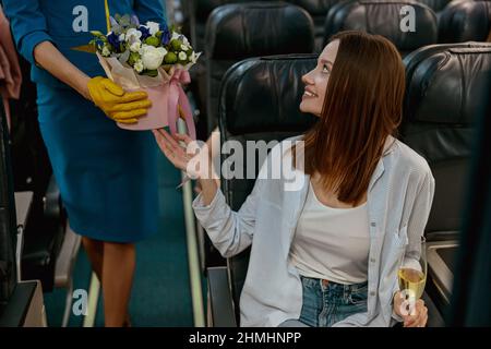 Femme joyeuse recevant des fleurs de l'hôtesse en avion Banque D'Images