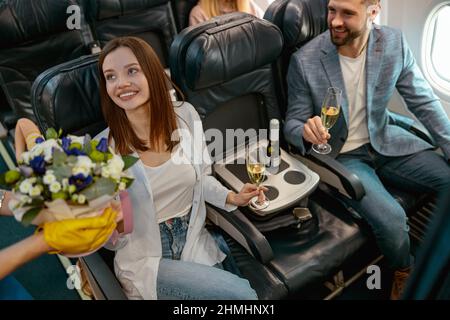 Femme joyeuse recevant des fleurs de l'hôtesse en avion Banque D'Images