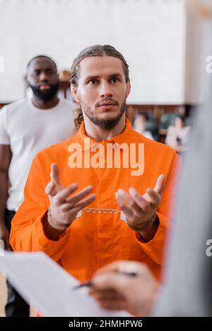 l'accusé est en uniforme de prison et les menottes gesturant près d'un procureur flou et d'un juré afro-américain devant un tribunal Banque D'Images