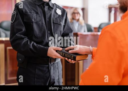 vue partielle de l'huissier en uniforme tenant la bible près de l'accusé prêtant serment devant le tribunal Banque D'Images