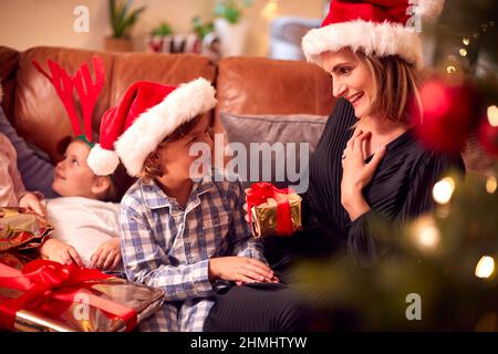 Le fils donne le cadeau de mère en famille assis sur un canapé à la maison ouvre les cadeaux de Noël Banque D'Images