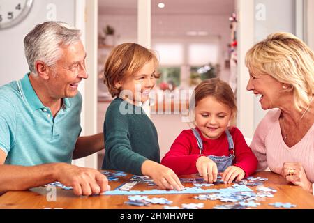 Petits-enfants avec grands-parents assis autour de la table à la maison faire le puzzle Jigsaw ensemble Banque D'Images