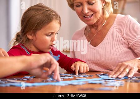 Petite-fille avec grand-mère assis autour de la table à la maison faire le puzzle Jigsaw ensemble Banque D'Images