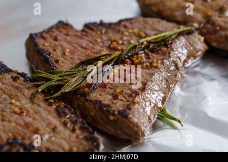 Trois steaks de bœuf rôtis avec des graines de romarin et de moutarde isolées sur du papier d'aluminium. Gros plan sur la viande grillée Banque D'Images