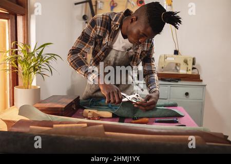 Un jeune artisan afro-américain fait des trous sur le cuir avec un perforateur en atelier Banque D'Images