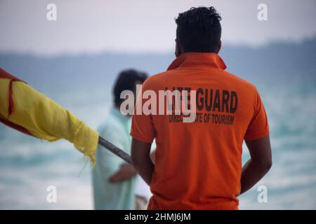 maître-nageur en chemise orange portant le drapeau le long de la plage avec des touristes en arrière-plan à havelock swaraj dweep andaman nicobar îles inde Banque D'Images