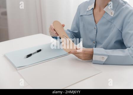 Médecin tenant une semelle intérieure tout en étant assis à une table.L'orthopédiste teste l'appareil médical.Semelles intérieures orthopédiques.Soins des pieds.Correction des pieds plats Banque D'Images