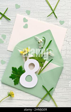 8 mars, Journée internationale de la femme. Enveloppe de bienvenue avec le numéro 8, fleurs en neige, coeurs sur table blanche. Banque D'Images