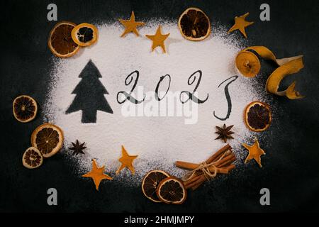 Arbre de Noël et 2023 tiré sur la farine dispersée sur fond noir, accessoires de cuisson et ingrédients. Joyeux Noël et bonne année 2023. Banque D'Images
