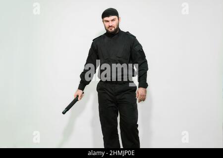 Défenseur. Mercenaire. Système BodyGuard. Homme de sécurité en uniforme noir avec un bâton dans ses mains sur fond blanc. Sécurité privée. Banque D'Images