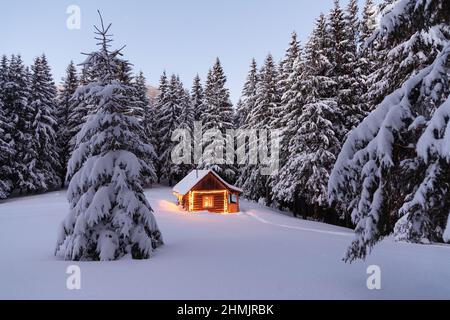 Les lampes éclaient la maison le soir. Paysage d'hiver. Cabane en bois sur la pelouse recouverte de neige. Nuit mystique. Mariez Noël et Nouveau Banque D'Images