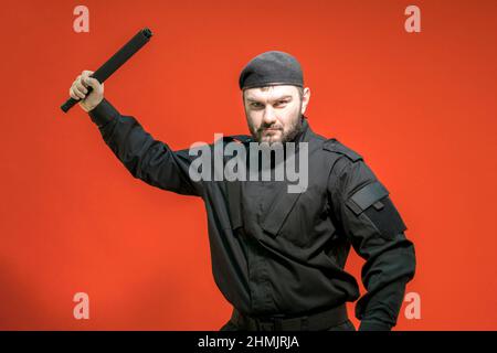 Mercenaire. Défenseur. Un garde mâle en uniforme noir et un chapeau ont pris une position défensive, tenant un bâton sur sa tête. Système BodyGuard. Sécurité privée. Banque D'Images