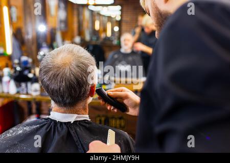 un maître tendance et élégant coupe les cheveux du client de l'homme ancien dans un salon de coiffure moderne Banque D'Images