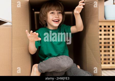 Garçon se cachant dans une énorme boîte en carton. Il joue et regarde hors d'une boîte. Un enfant est heureux de s'installer dans une nouvelle maison. Banque D'Images