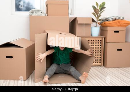 Un petit garçon excité sautant à l'intérieur d'une énorme boîte en carton. Il joue et regarde hors d'une boîte. Un enfant est heureux de s'installer dans une nouvelle maison. Banque D'Images