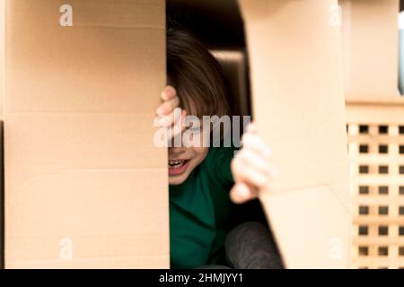 Garçon se cachant dans une énorme boîte en carton. Il joue et joue à travers un trou dans la boîte. Un enfant est heureux de s'installer dans une nouvelle maison. Banque D'Images