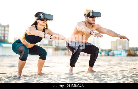 Un couple de femmes moderne qui s'accroupient à la plage avec un casque vr Goggle - concept sportif et technologique de style de vie avec des personnes en forme physique qui s'exercent sur Quest simul Banque D'Images