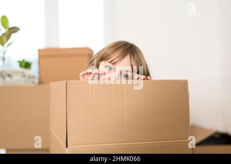 Un petit garçon excité sautant à l'intérieur d'une énorme boîte en carton. Il joue et regarde hors d'une boîte. Un enfant est heureux de s'installer dans une nouvelle maison. Banque D'Images