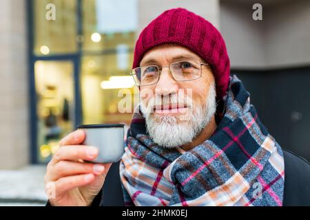 goog regardant l'homme mûr boire le thé chaud dans la rue de la ville en hiver Banque D'Images