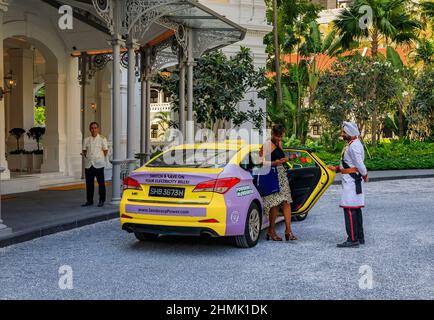 Singapour - 08 septembre 2019 : une femme noire sort d'un taxi à l'emblématique hôtel Raffles, assistée par le portier Sikh dans un uniforme militaire Banque D'Images