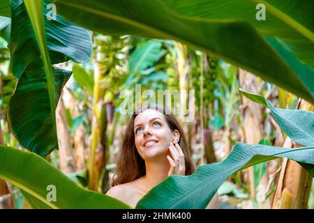 Beau jeune caucasien brunette long cheveux femme portrait près de la banane paume feuilles des plantes tropicales dans la jungle. Soins de la peau et beauté naturelle biologique Banque D'Images