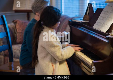 South Jordan, Utah, États-Unis, 10 février 2022. Une belle jeune étudiante de piano se concentre sur sa leçon. Son professeur la surveille à chaque mouvement. Banque D'Images