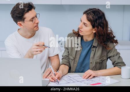 Le couple est assis dans la cuisine boissons café pour le petit-déjeuner et parle de dessins de rénovation d'appartement faire des notes dans l'ordinateur portable et le bloc-notes Banque D'Images