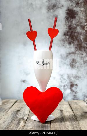 Concept de la Saint-Valentin. Verre de champagne avec pailles à boire et coeur en peluche rouge sur une table en bois. Mise au point sélective. Banque D'Images