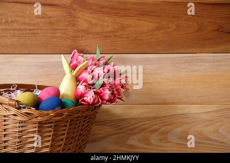 Panier en osier avec œufs de Pâques et fleurs sur fond de bois Banque D'Images