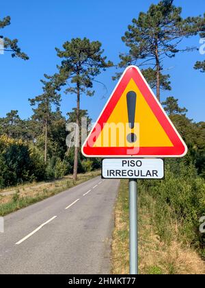 Panneau d'avertissement de chaussée bosselée avec un point d'exclamation dans un triangle rouge sur fond jaune. Route à travers la forêt. Banque D'Images