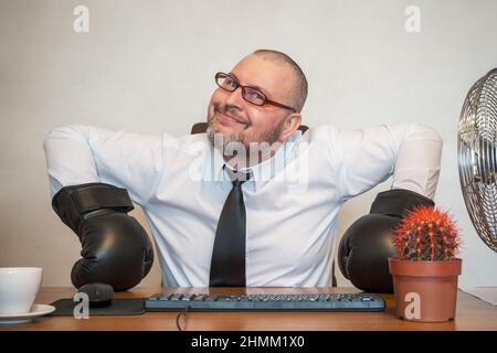 L'homme décrit comiquement le travail d'un homme d'affaires. Il est assis à une table portant des gants de boxe. Banque D'Images