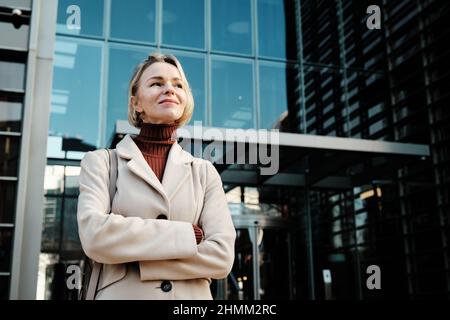 Une femme d'affaires confiante posant avec ses armes a croisé un immeuble de bureaux dans le quartier financier de la ville. Banque D'Images