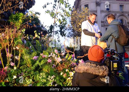 Des plantes et des fleurs couvrent la fontaine commémorative Shaftesbury, souvent connue sous le nom d'« Eros », à Piccadilly Circus, Londres, Royaume-Uni. Pour une journée le 10th février 2022, cette annonce a annoncé une expérience de réalité augmentée Green Planet qui a ouvert ses portes à Piccadilly Circus le 11th février 2022. Parmi les partenaires et les partisans de ce projet figurent BBC Earth, EE, Crown Estate, Factory 42, Kew Royal Botanic Gardens, Talesmith et dimension. 2022. Adam, ambassadeur du projet, se tient devant la statue, prêt à informer les passants et à donner des paquets de graines gratuits. Banque D'Images