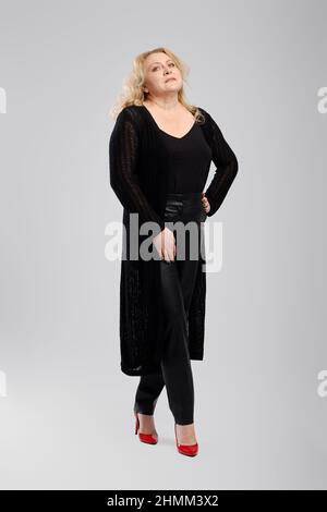 Photo du corps de la vieille femme heureuse dans un gilet tricoté et un pantalon en similicuir sur fond gris studio Banque D'Images