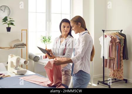 Deux tailleurs féminins travaillent sur une tablette pour créer une nouvelle ligne de vêtements Banque D'Images