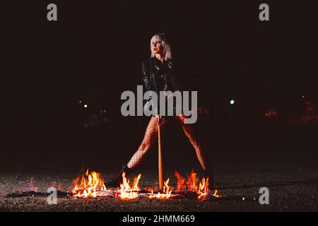 Portrait de la jeune femme blonde élégante grunge avec le club près du feu Banque D'Images