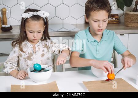 Portrait de deux petits enfants concentrés, un garçon, une fille, des oeufs de poules de Pâques multicolores. Trempage, cuillère à œufs animaux de couleur absorbants, bols. Papier Banque D'Images