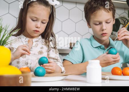 Portrait de deux enfants studieusement joyeux, petit garçon et fille, pinceau multi coloriage poules oeufs sur table en papier. Faire de l'art blanc Banque D'Images