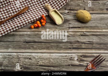 Composition sur une table de cuisine rustique en bois composée de coutellerie en bois, de farine et de pomme de terre biologique.fond alimentaire.Ingrédients pour faire des recettes saines. Banque D'Images