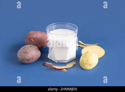 Un verre transparent avec du lait de pomme de terre végétale sur une table bleue près des tubercules de pomme de terre.Gros plan sur le lait sans lactose à base de plantes végétaliennes.Une alimentation saine et Un Banque D'Images