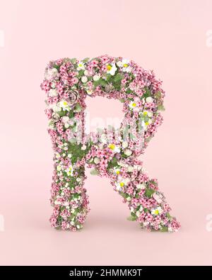 Concept R de la lettre créative fait de fleurs fraîches de mariage de printemps. Concept de police de fleurs sur fond rose pastel. Banque D'Images